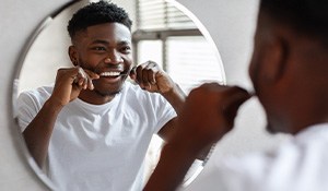 Man smiling while flossing his teeth in bathroom