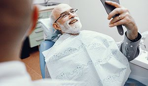 Man smiling at dental office looking into hand mirror