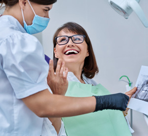 Woman smiling with dentist while reviewing X-ray