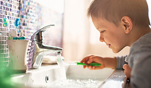 young boy washing toothbrush