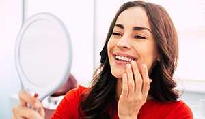 A woman admiring her dental implants in a hand mirror