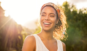 A young woman wearing a white tank top and smiling while standing outside and enjoying the sun