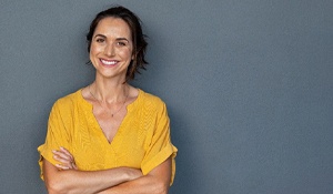 A woman wearing a yellow blouse stands with her arms folded and showing off her improved smile