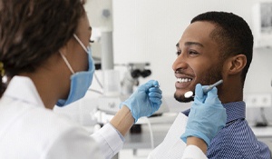 A female periodontist examines a young man’s smile during an appointment	