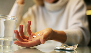 Person holding pills by glass of water