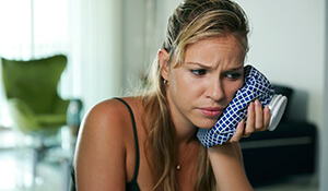 Pained woman holding ice pack on cheek