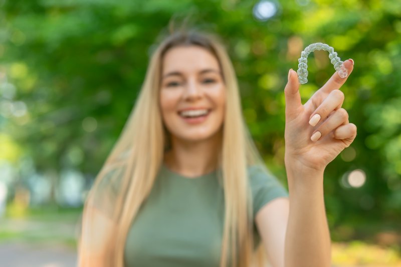 A blurred woman holding an Invisalign tray in a summer setting